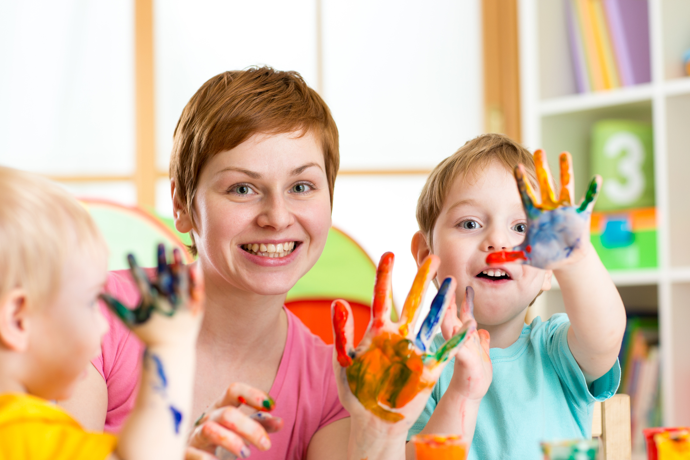Erzieherin spielt malt mit Fingerfarben mit Kindern