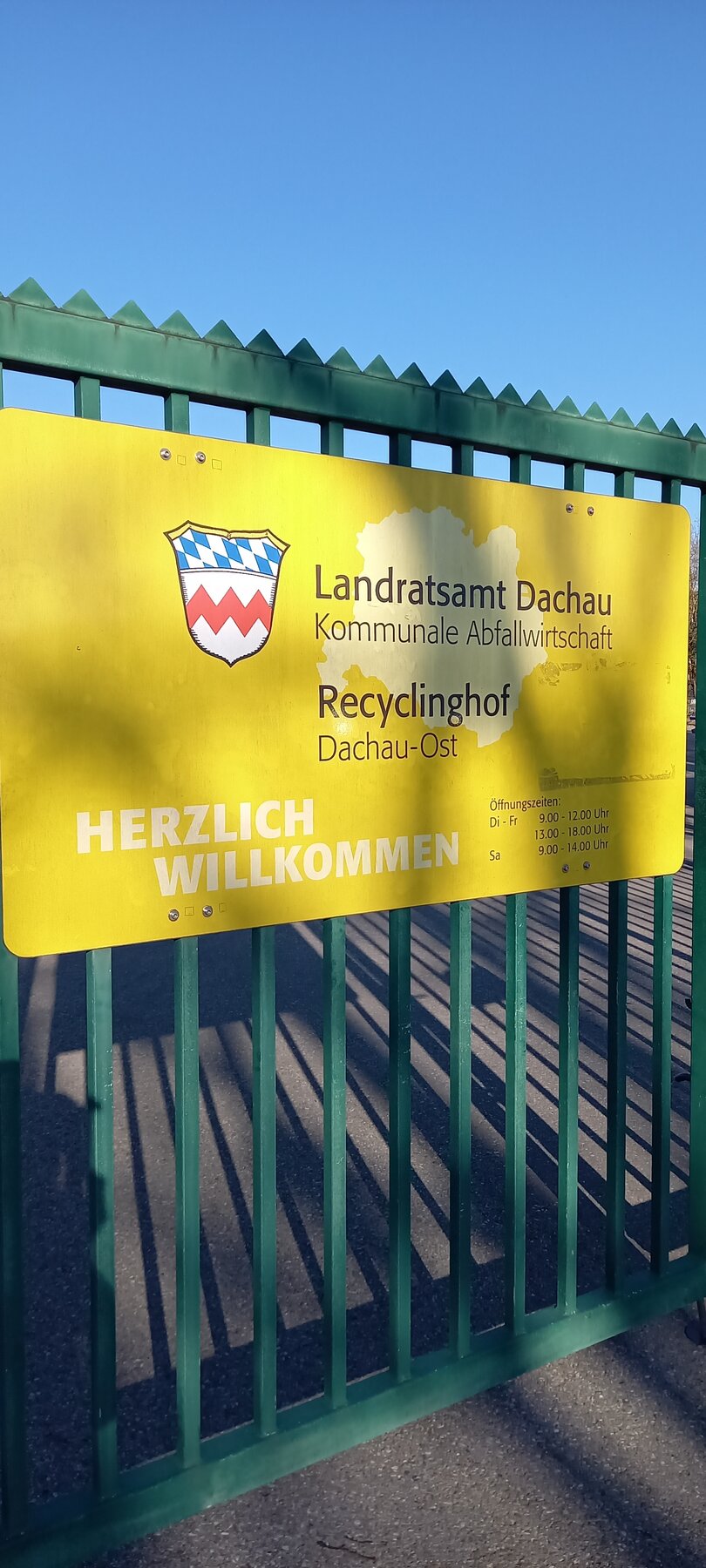 An einem Tor ist ein Schild angebracht mit den Öffnungszeiten des Recyclinghofs Dachau-Ost