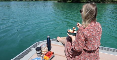 Eine Frau sitzt am Wasser mit Essen und Getränken