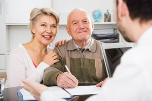 Älteres Paar unterschreibt Unterlagen, während eine Person etwas erklärt.